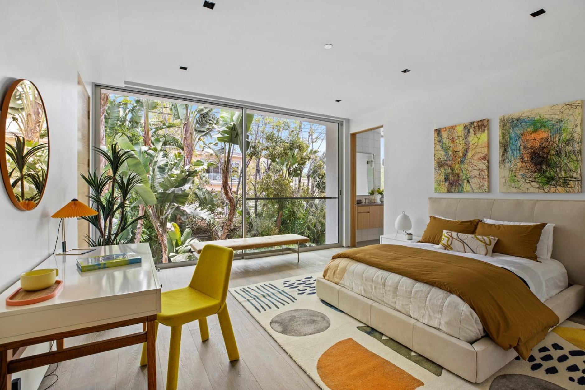 Vibrant bedroom with harmonious palette, colorful decor, desk space, circular mirror, and nature-filled backdrop.