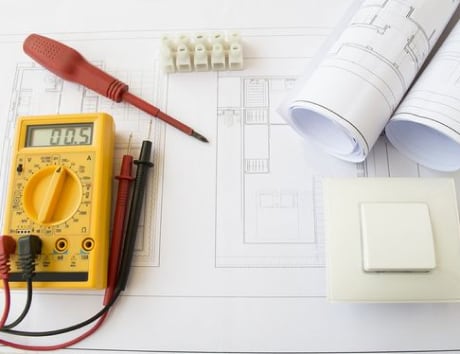 A table covered in floor plan drawings and a multimeter, illustrating the meticulous planning and implementation of smart energy management solutions.