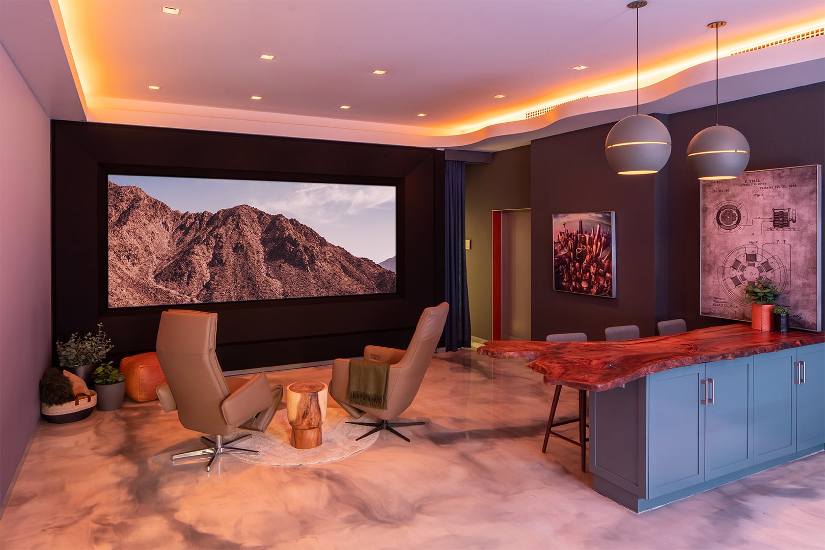 In a warm orange-lit setting, the Global Wave Showroom presents a captivating mountain view on its theater screen, while luxurious chairs face the display, and a meticulously crafted wooden island takes center stage.