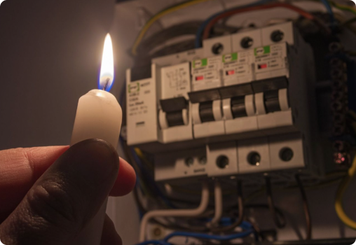 A hand holds a lit candle stick up to an open electrical box.